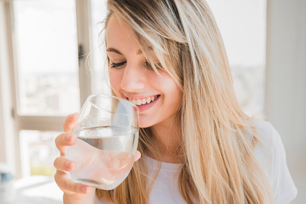 Une femme blonde qui boit dans un verre parfaitement propre.
